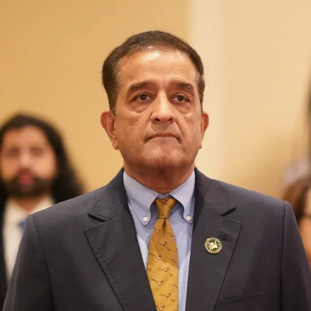 Malik Amin Aslam, International Liaison of the chapter, stands in a navy blazer and gold tie at a gala.