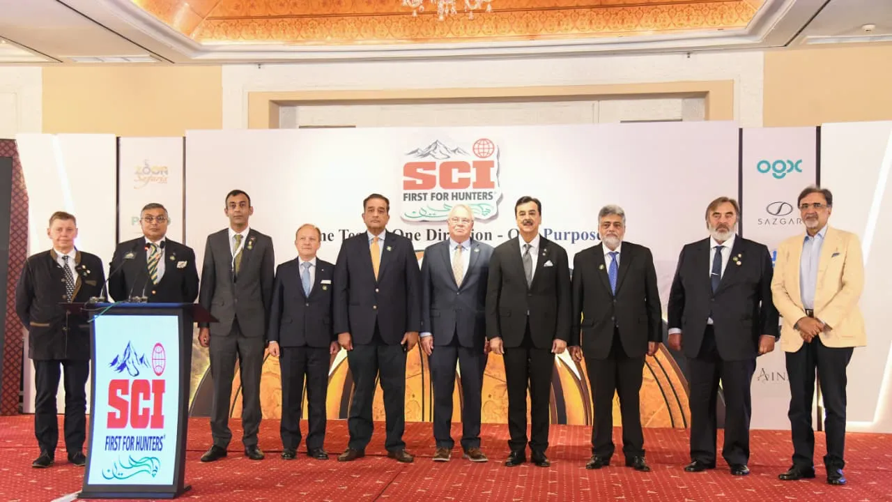 Ten chapter members and visiting SCI delegates stand in a row on a red-carpeted stage beside an SCI First for Hunters lectern.