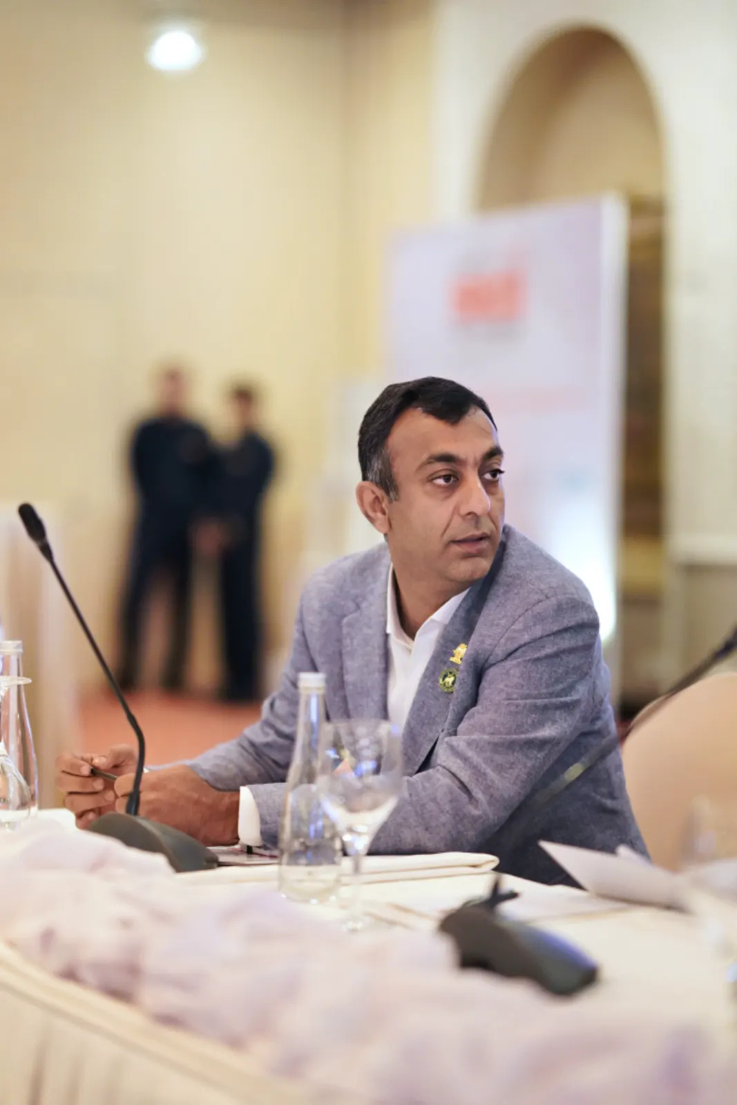 A delegate in a grey jacket listens at the conference table.