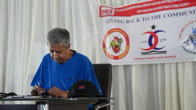 A doctor in blue scrubs writes at a table beneath a "Giving back to the communities" banner at the chapter’s medical camp.