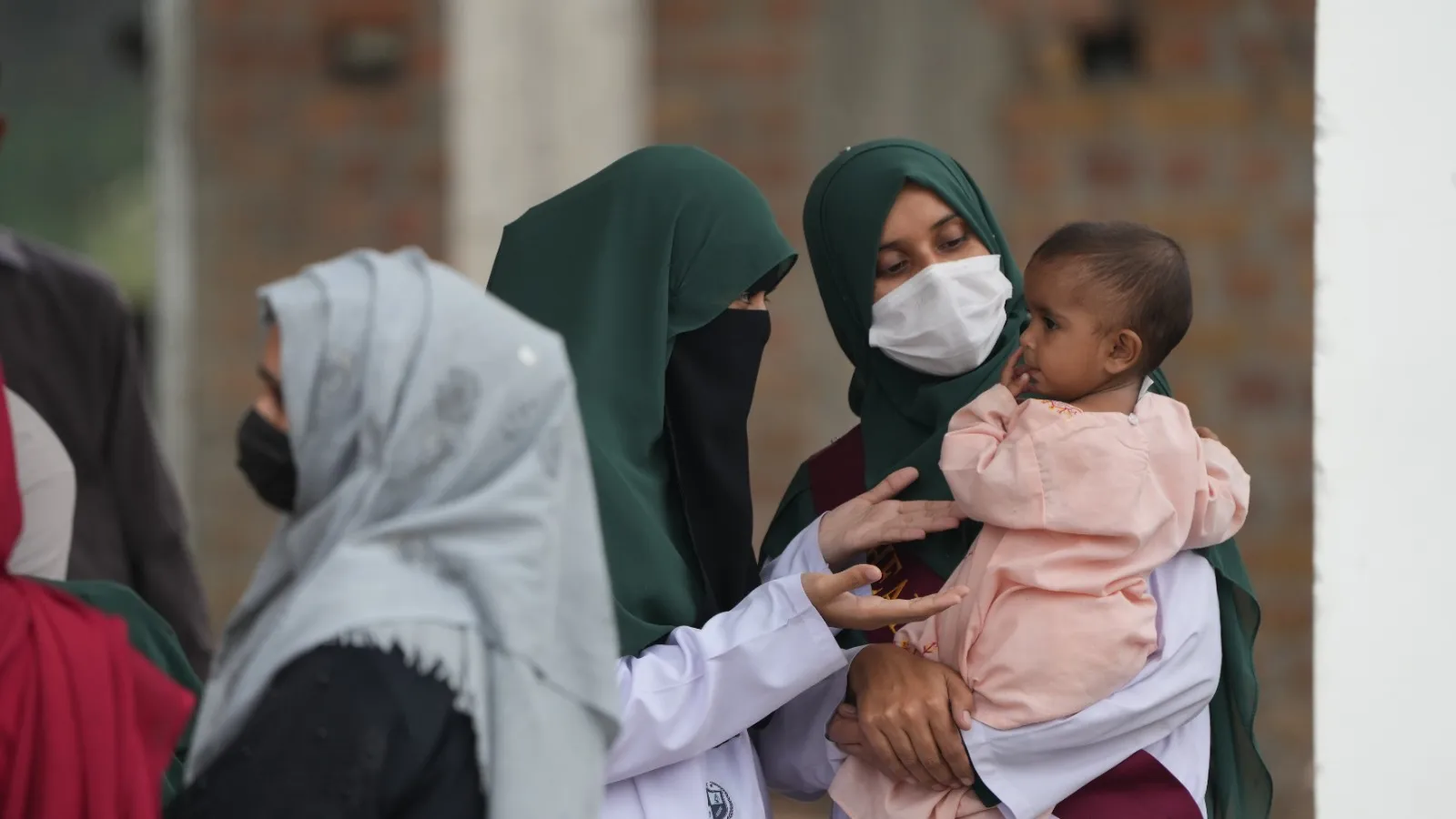A doctor in a white coat and a mother holding a toddler at the medical camp.