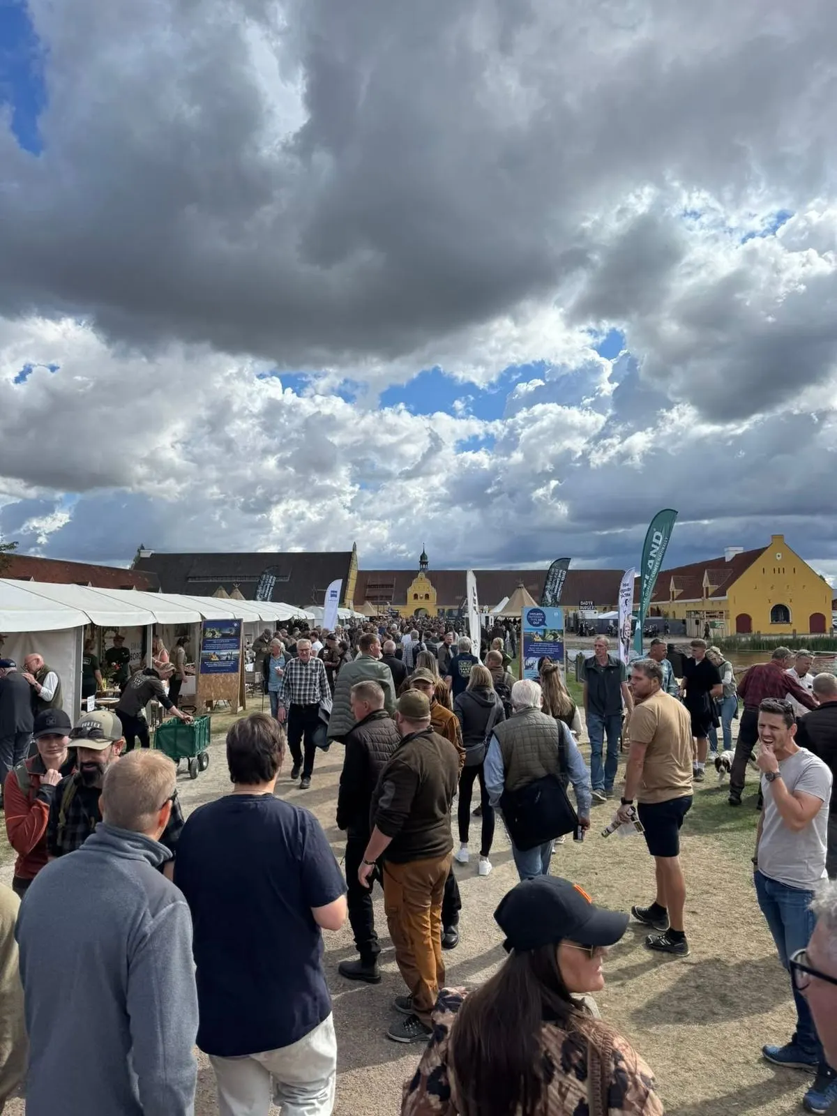 Visitors crowd an outdoor nature fair under a wide, cloudy sky.
